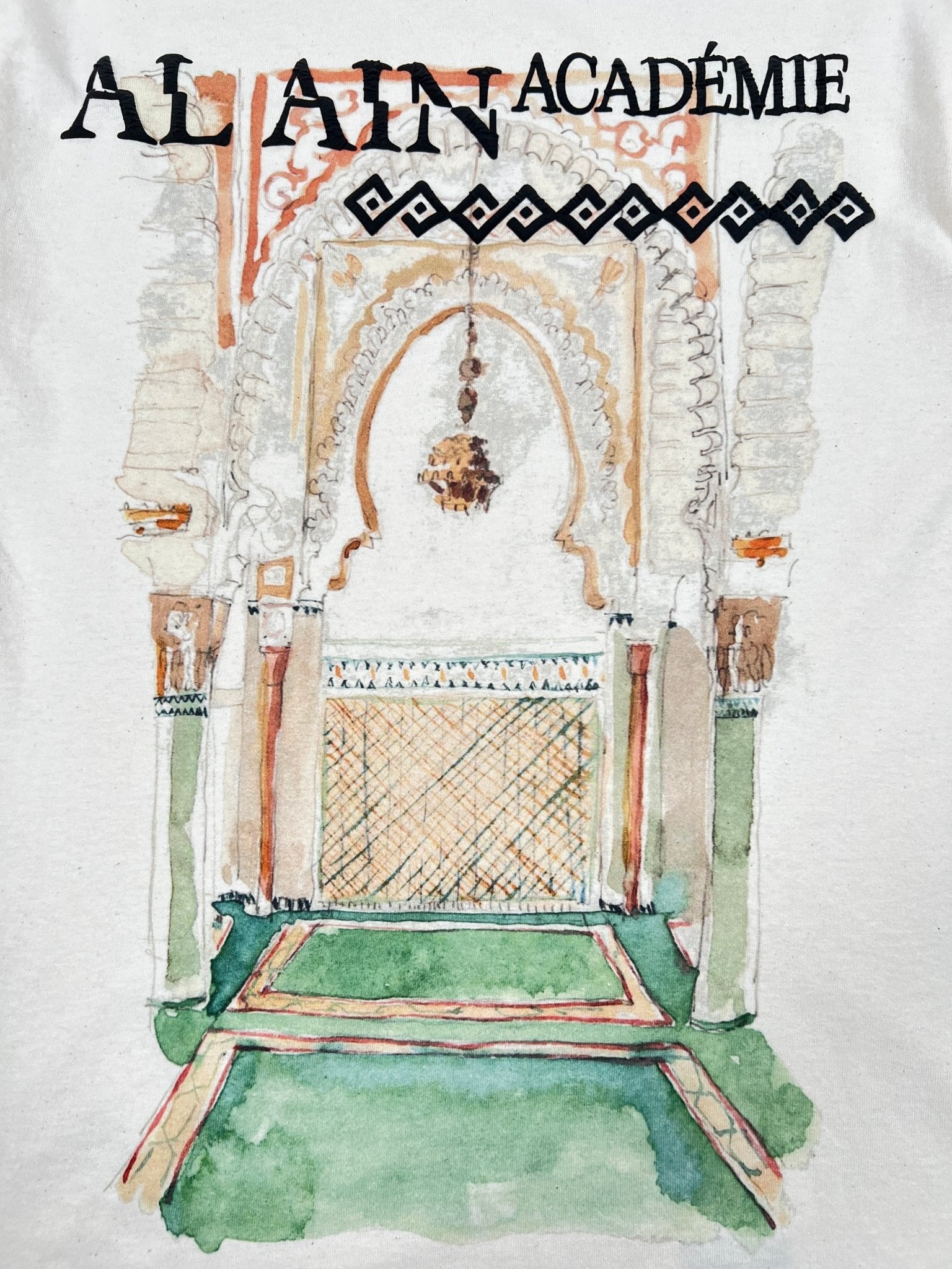 The Al Ain AMHX-S821 Makan T-shirt by AL AIN features a watercolor arched doorway with lantern, tiled decor, and "AL AIN ACADÉMIE" text. Made in Italy from 100% cotton in a natural finish.