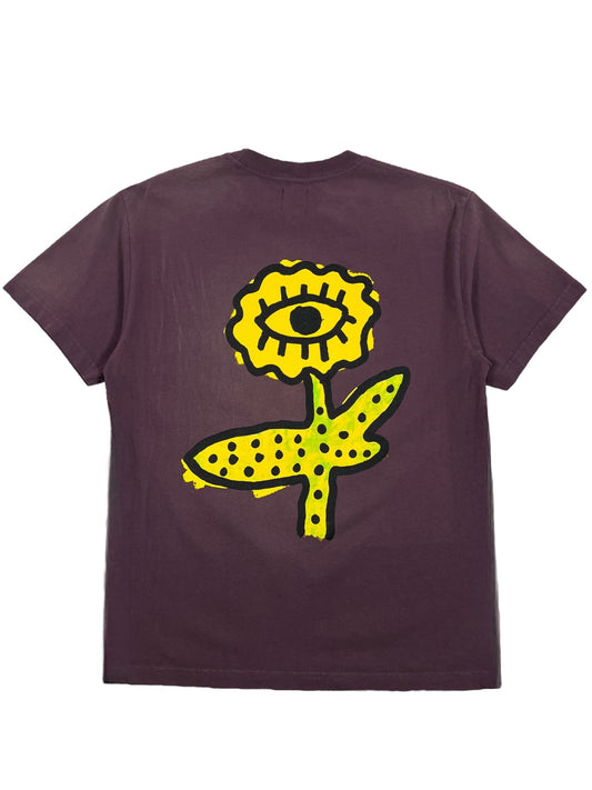 The Alchemist All-Seeing Cactus Tee Plum by ALCHEMIST, crafted from 100% cotton, features a distinctive vintage washed finish with a prominent yellow flower and eye design boldly printed on the back.