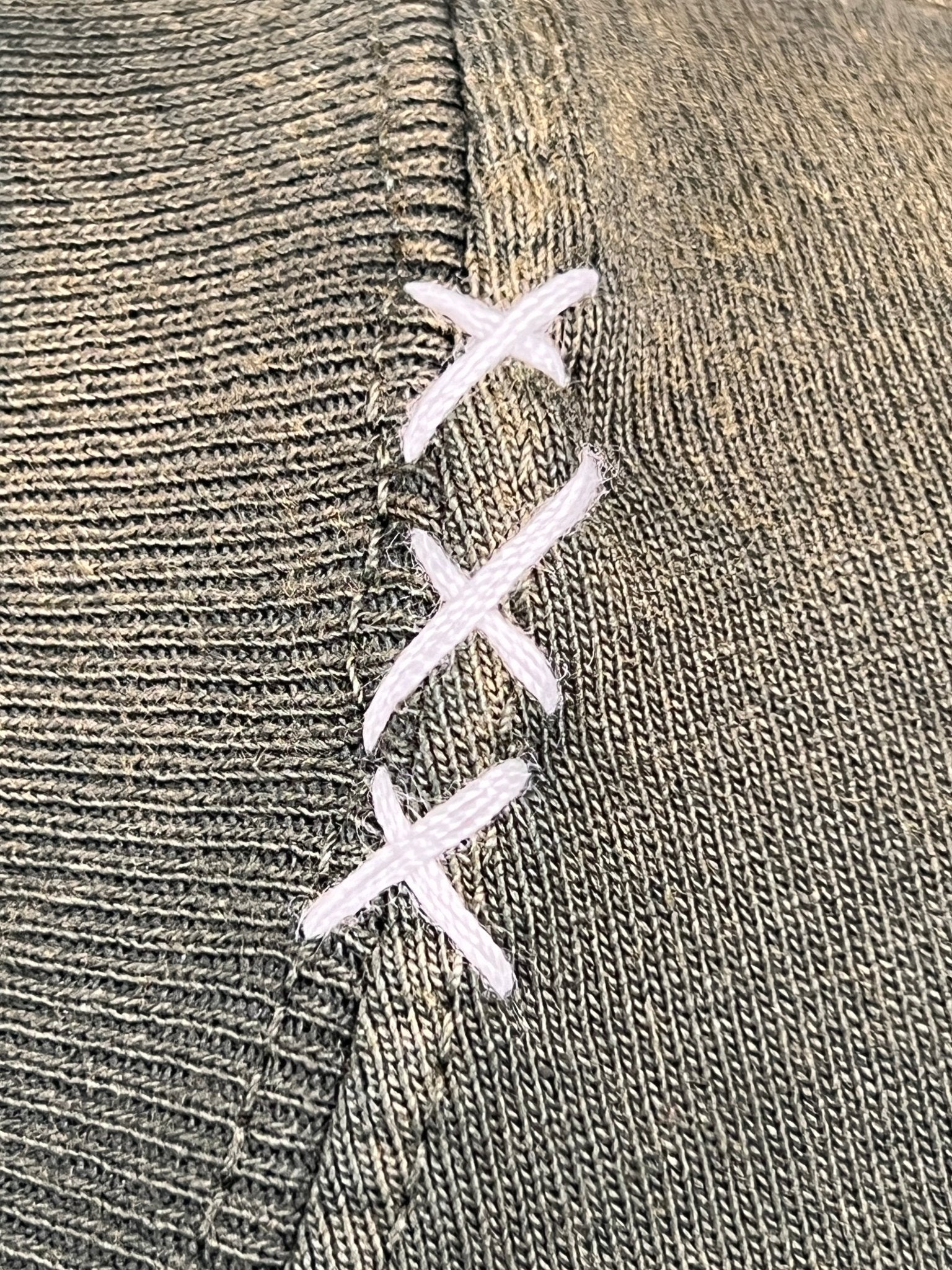 Close-up of an ALCHEMIST BLOCK PRINT S/S TEE MOSS GREEN repairing a tear near the seam, showcasing its intricate design and quality craftsmanship.