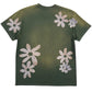 The ALCHEMIST BLOCK PRINT S/S TEE in moss green is a vintage-washed T-shirt adorned with large, light-colored flower designs on the back and sleeves, ideal for those who appreciate a classic graphic tee.