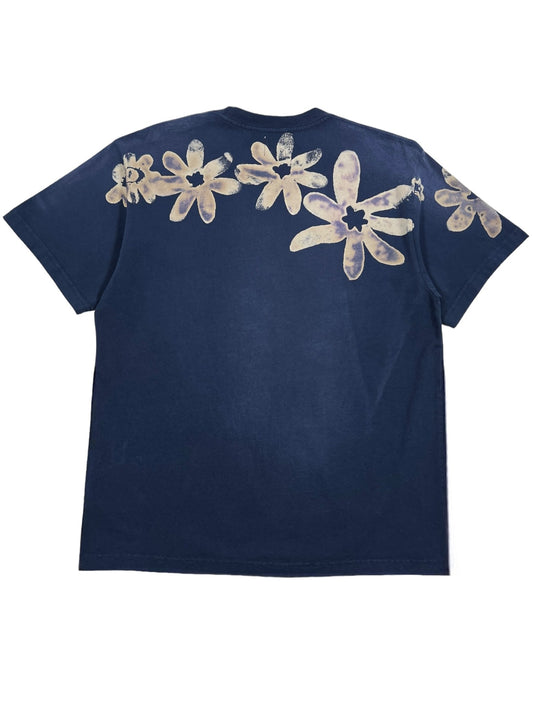 The Alchemist Block Print S/S Tee in Nightfall Blue by ALCHEMIST features large beige flower patterns along the upper back and a vintage washed finish for a timeless look.