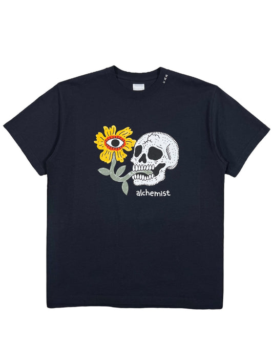 The Alchemist Floral Skull Tee 2 Black from ALCHEMIST features a vintage washed finish and displays a graphic of a sunflower with an eye in the center alongside a skull, with "ALCHEMIST" prominently printed below.