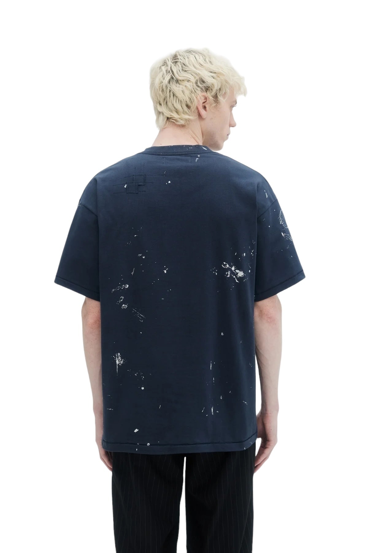 A person with blonde hair wears a Domrebel Atelier Pocket Tee in dark blue and black pants, showcasing an edgy fashion style while facing away from the camera.