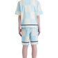 A person wears the Barrow S5BWUABE074 Popeline Shorts in vanilla, paired with a blue and cream checkered shirt. They stand with their back to the camera, sporting black boots and socks.