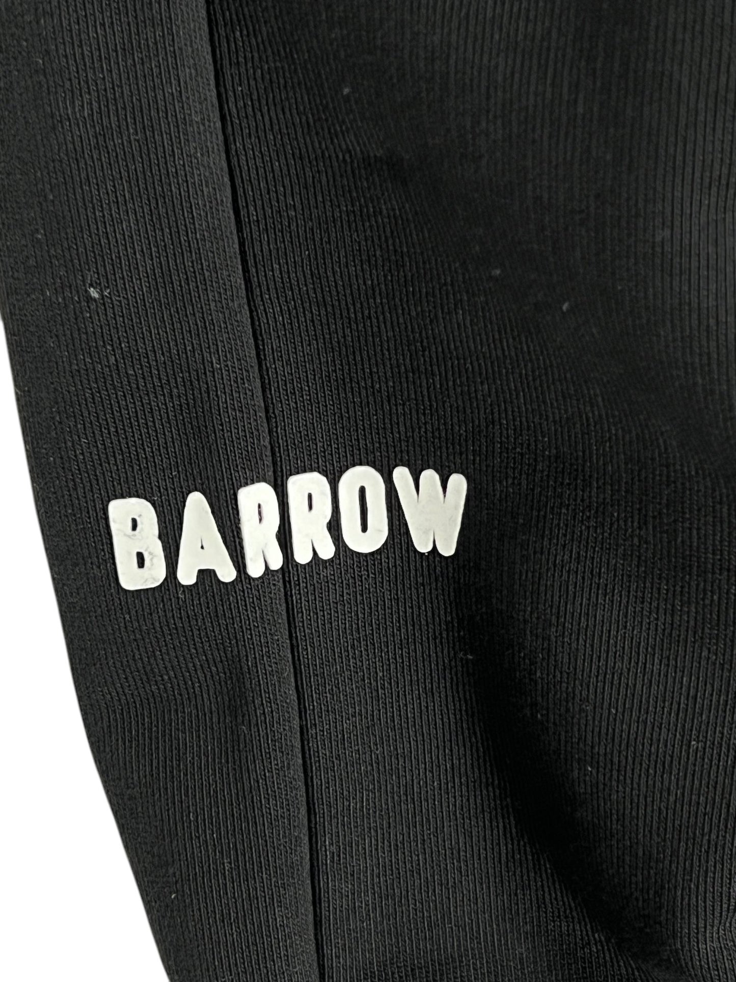 Close-up of Barrow S5BWUAFP025 Sweatpants Nero/Black featuring the word "BARROW" in white, raised letters on black fabric. Crafted from 100% cotton, this piece showcases quality and Italian craftsmanship.