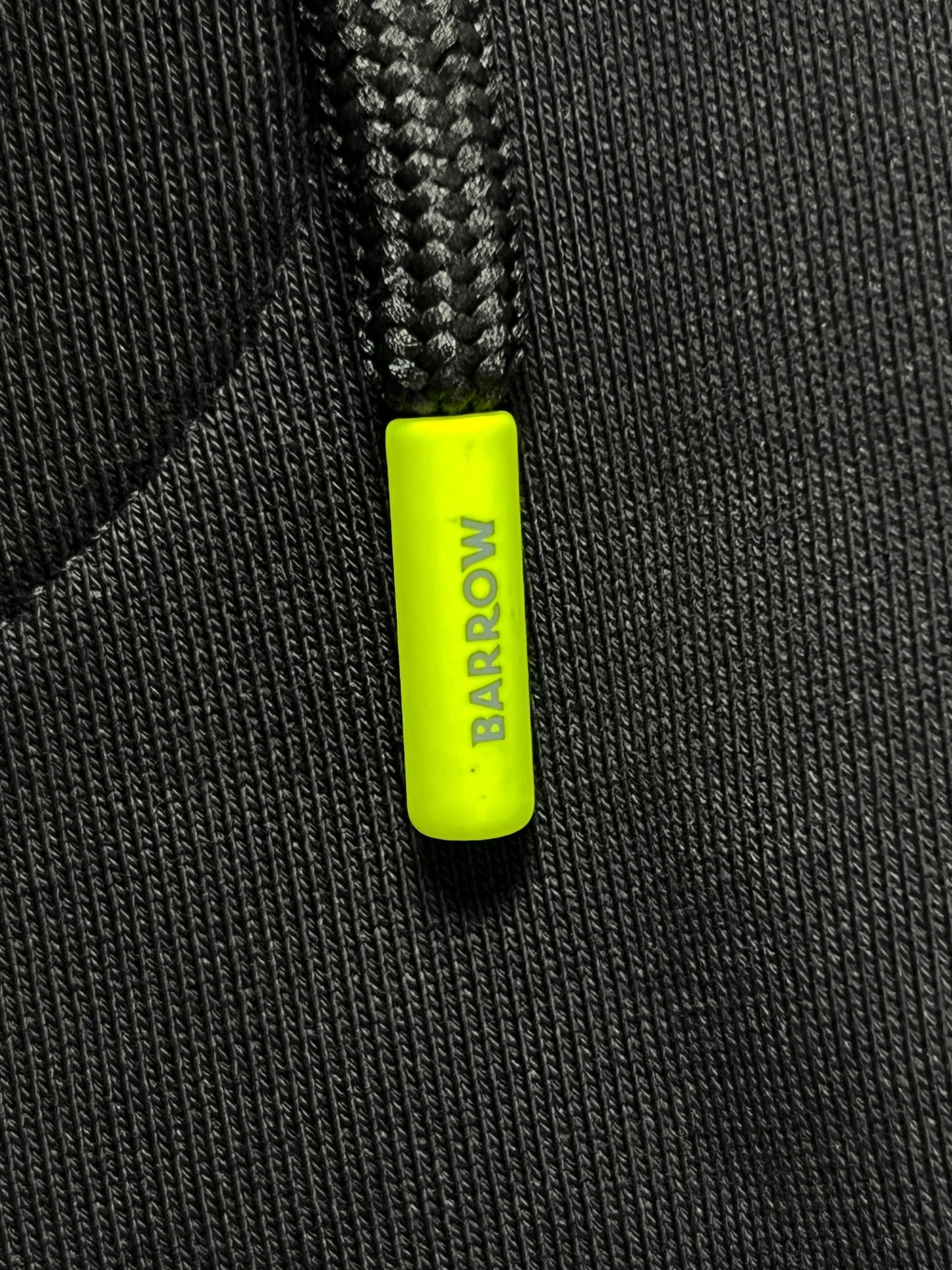 Close-up of Barrow S5BWUAFP025 Sweatpants Nero/Black by BARROW, showcasing black textured cotton fabric with a yellow drawstring toggle labeled "BARROW," exuding a premium sweatpants style. Made in Italy, highlighting exquisite craftsmanship.