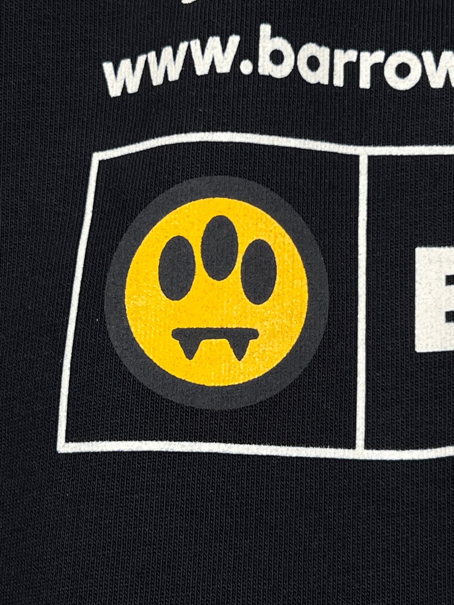 Close-up of the Barrow S5BWUAHS063 Hoodie, featuring a black fabric with a distinct yellow paw print and fangs design encircled. "www.barrow" is partially visible above the motif, highlighting its unique style. Crafted from 100% cotton by BARROW.