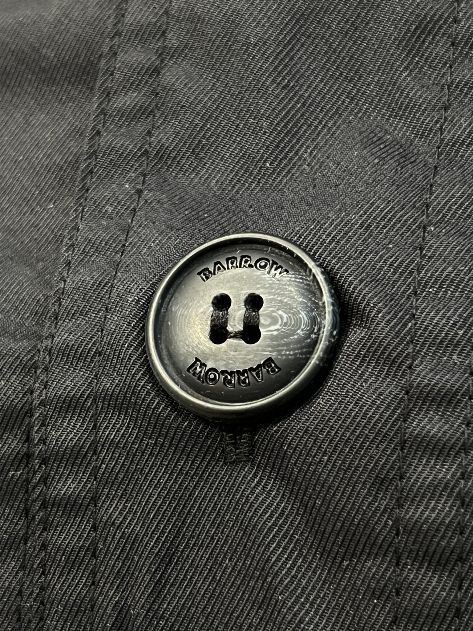 Close-up of a black button engraved twice with "BARROW," sewn onto the Barrow S5BWUAJK065 Unisex Jacket in Nero/Black—showcasing perfect detail and urban style.