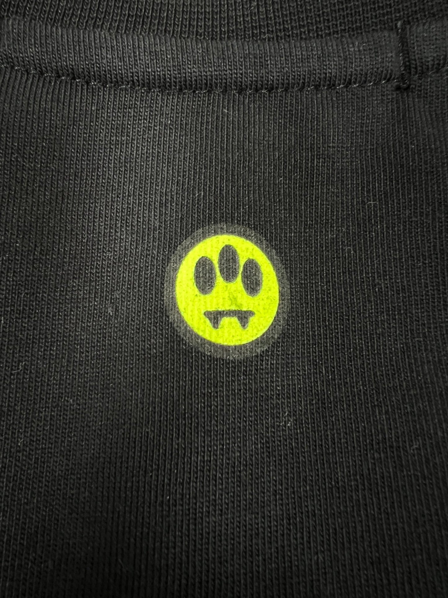 The sleek fabric surface of the Barrow S5BWUATH022 Jersey T-shirt Nero/Black by BARROW features a small yellow circle with a black paw print and fangs design, reminiscent of a football jersey.