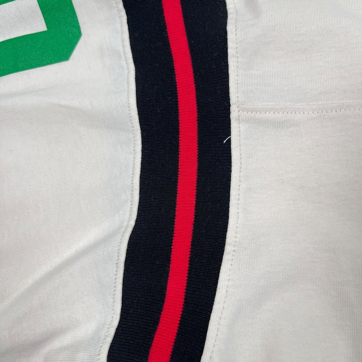 Close-up of the Barrow S5BWUATH032 Jersey T-shirt Vanilla, featuring a black and red stripe on a white background, similar to a Barrow football jersey, placed beside a green numeral or letter.