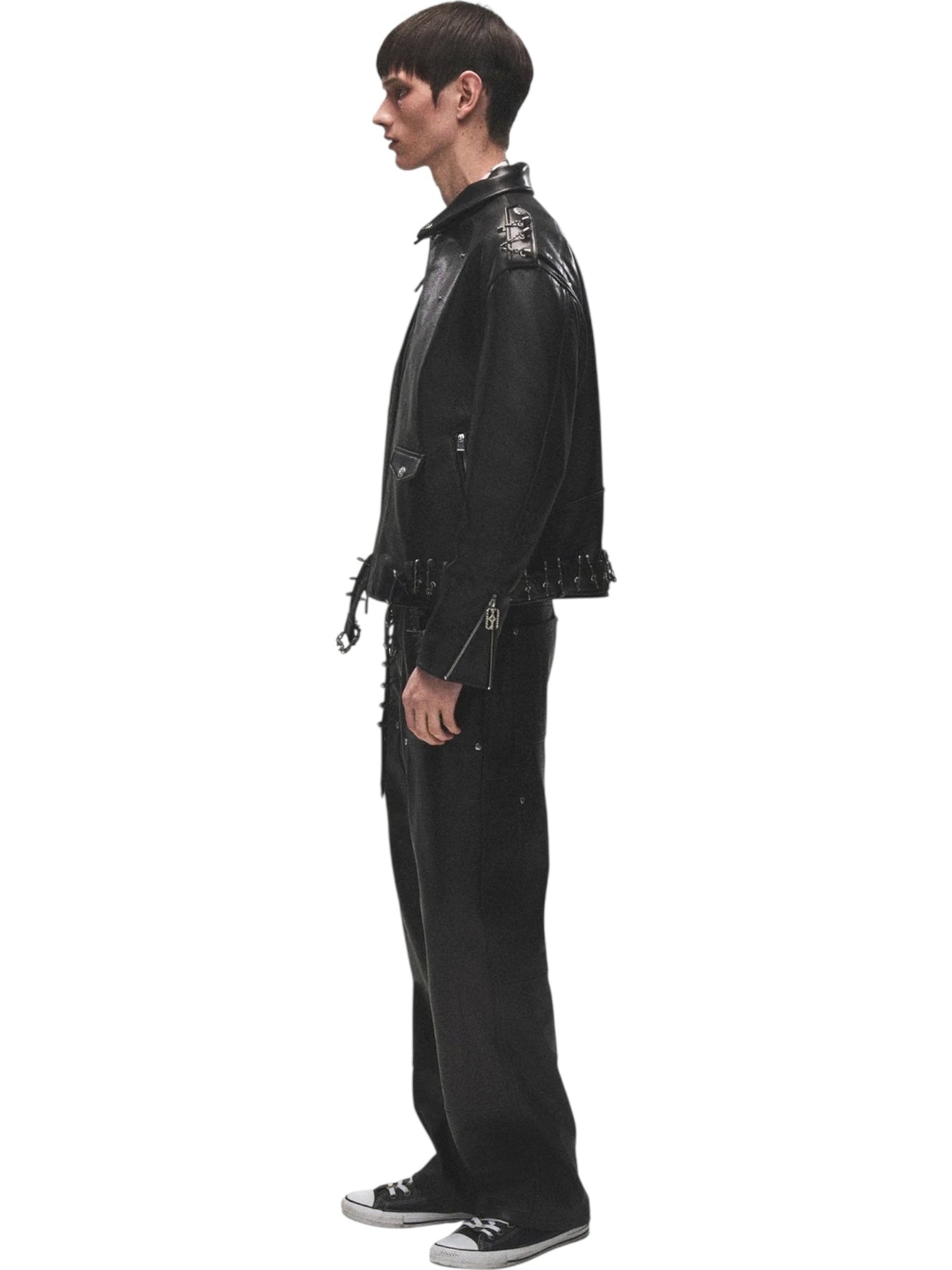 A person stands in profile against a white background wearing the BIRTH OF ROYAL CHILD Birth Of Royal Child BC25SSJK09 Pin Detail Leather Jacket in black, paired with matching black pants and sneakers.