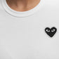 Person wearing a Comme des Garcons P1T801 T-SHIRT RHINESTONE HEART WHT/BLK by COMME DES GARCONS X PLAY, featuring a black heart patch with eyes and rhinestone border on the left chest.