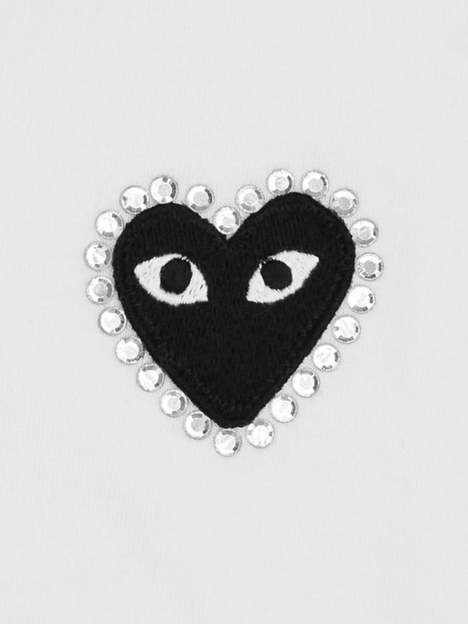 The COMME DES GARCONS X PLAY P1T801 T-SHIRT features a black embroidered heart-shaped patch with white eyes, outlined in shiny rhinestones, set on a plain white background.