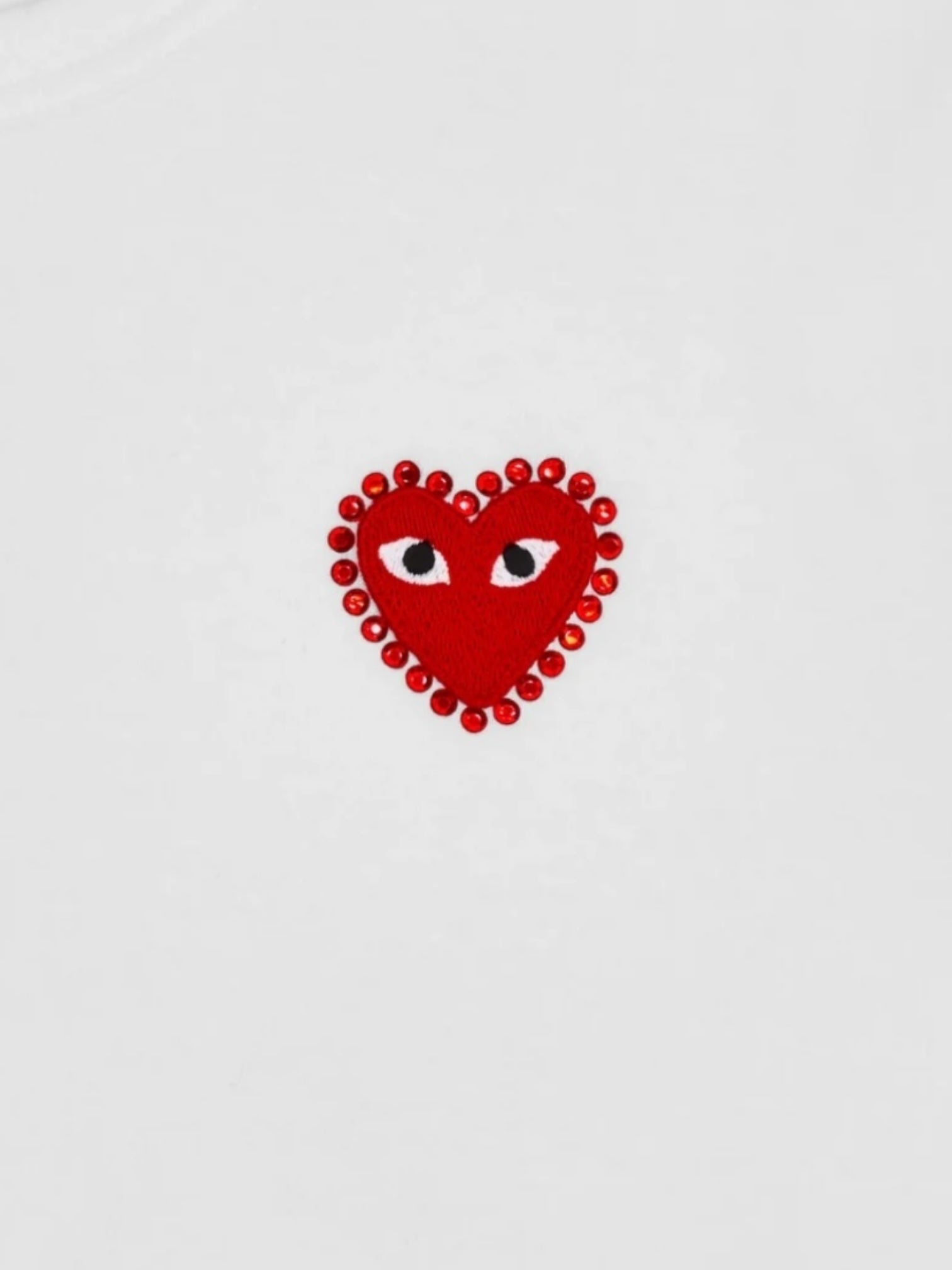The COMME DES GARCONS X PLAY P1T801 T-Shirt features a white base with a red rhinestone heart adorned with two eyes and a dotted border, inspired by the classic CDG design.
