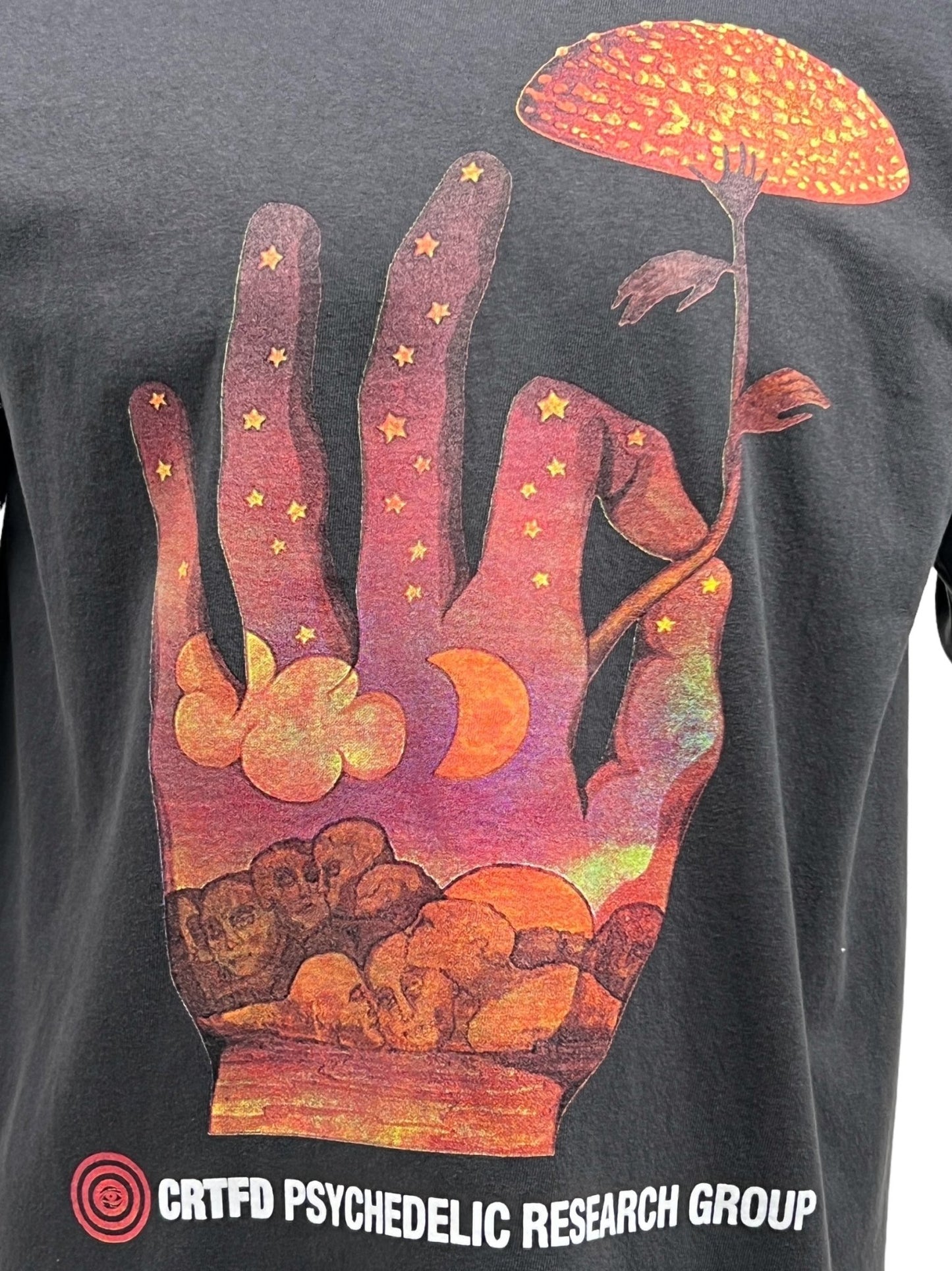 The CRTFD FLY AGARIC T-SHIRT in Vintage Black is crafted from organic cotton and showcases a captivating psychedelic design. It features a hand, starry sky, clouds, moon, and mushroom, with "CRTDF PSYCHEDELIC RESEARCH GROUP" text at the bottom. Ideal for fans of unique graphic t-shirts.