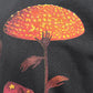 Get your hands on the CRTFD FLY AGARIC T-SHIRT VINTAGE BLK by CRTFD, showcasing a print of a humanoid figure with a mushroom cap as its head, set against a dark background and featuring vibrant orange and yellow hues. Crafted from soft organic cotton, this graphic tee is both eco-friendly and stylish.