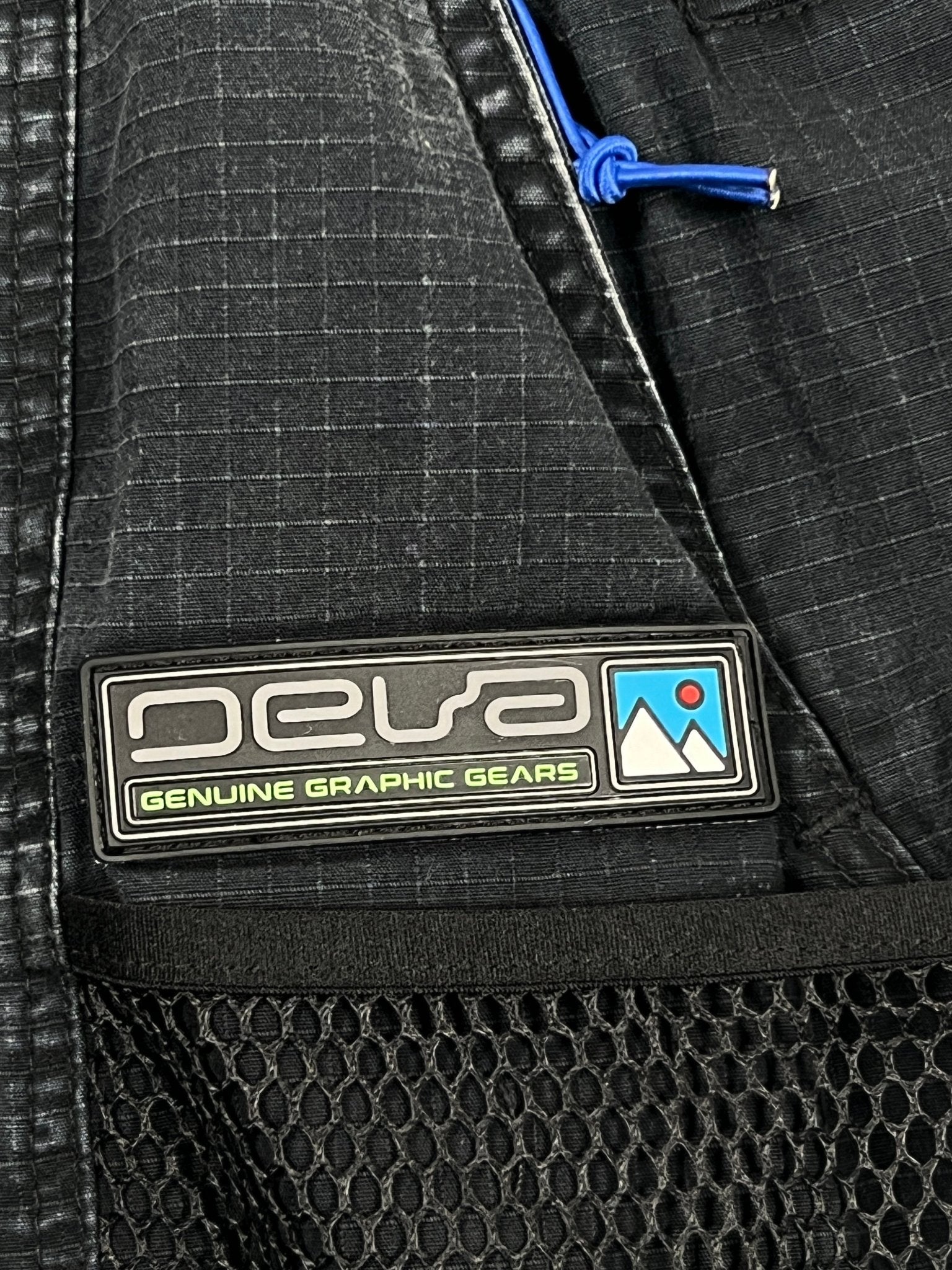 Close-up of DEVA'STATES Deva'States Hike Cargo Shorts in washed black, featuring a branded patch, adjustable webbing belt, and blue cord detail above the mesh pocket.