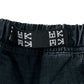 Close-up of the black elastic waistband on DEVA'STATES Deva'States Hike Cargo Shorts Washed Black, featuring a woven black and white label with geometric patterns.