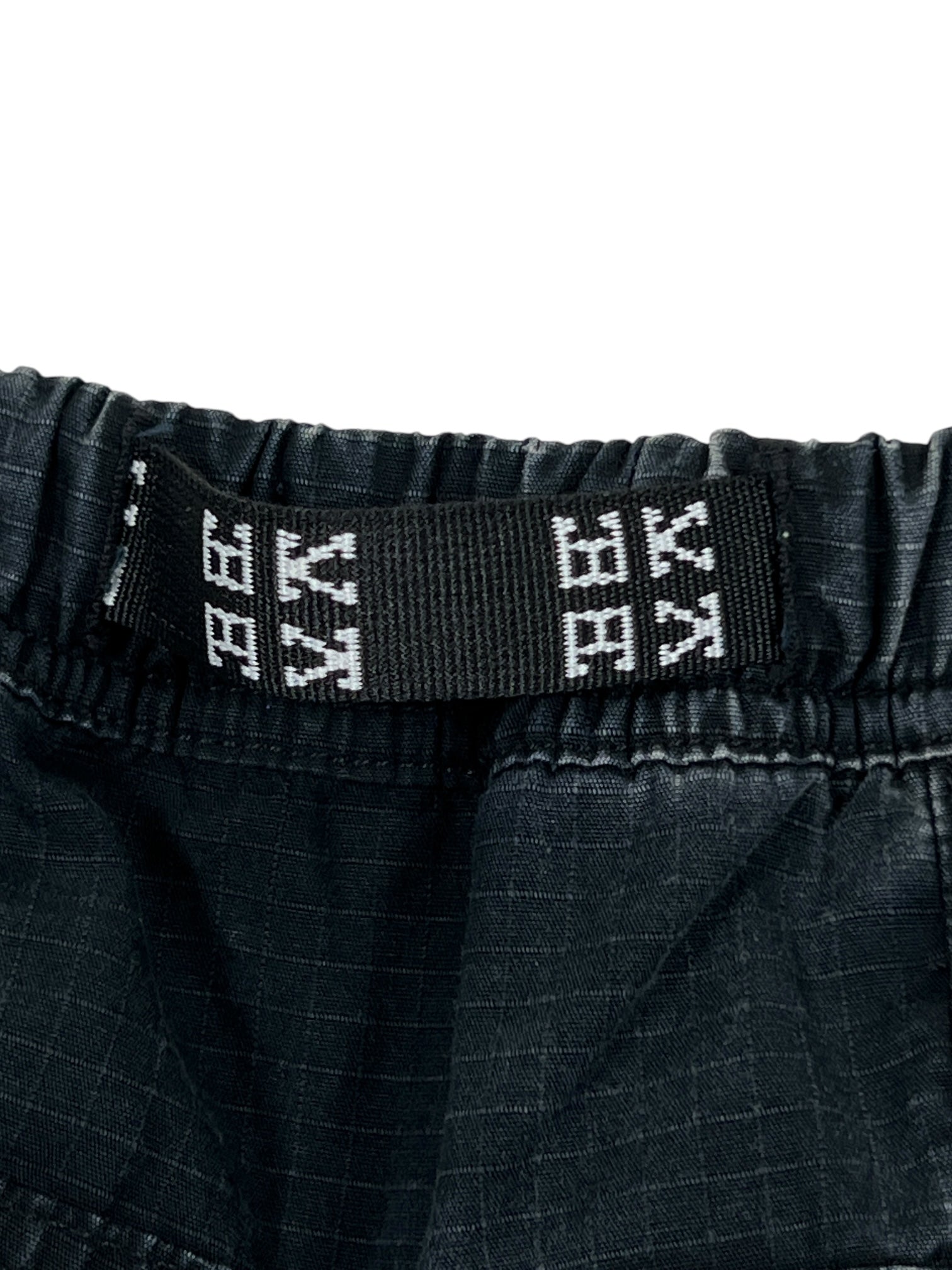 Close-up of the black elastic waistband on DEVA'STATES Deva'States Hike Cargo Shorts Washed Black, featuring a woven black and white label with geometric patterns.
