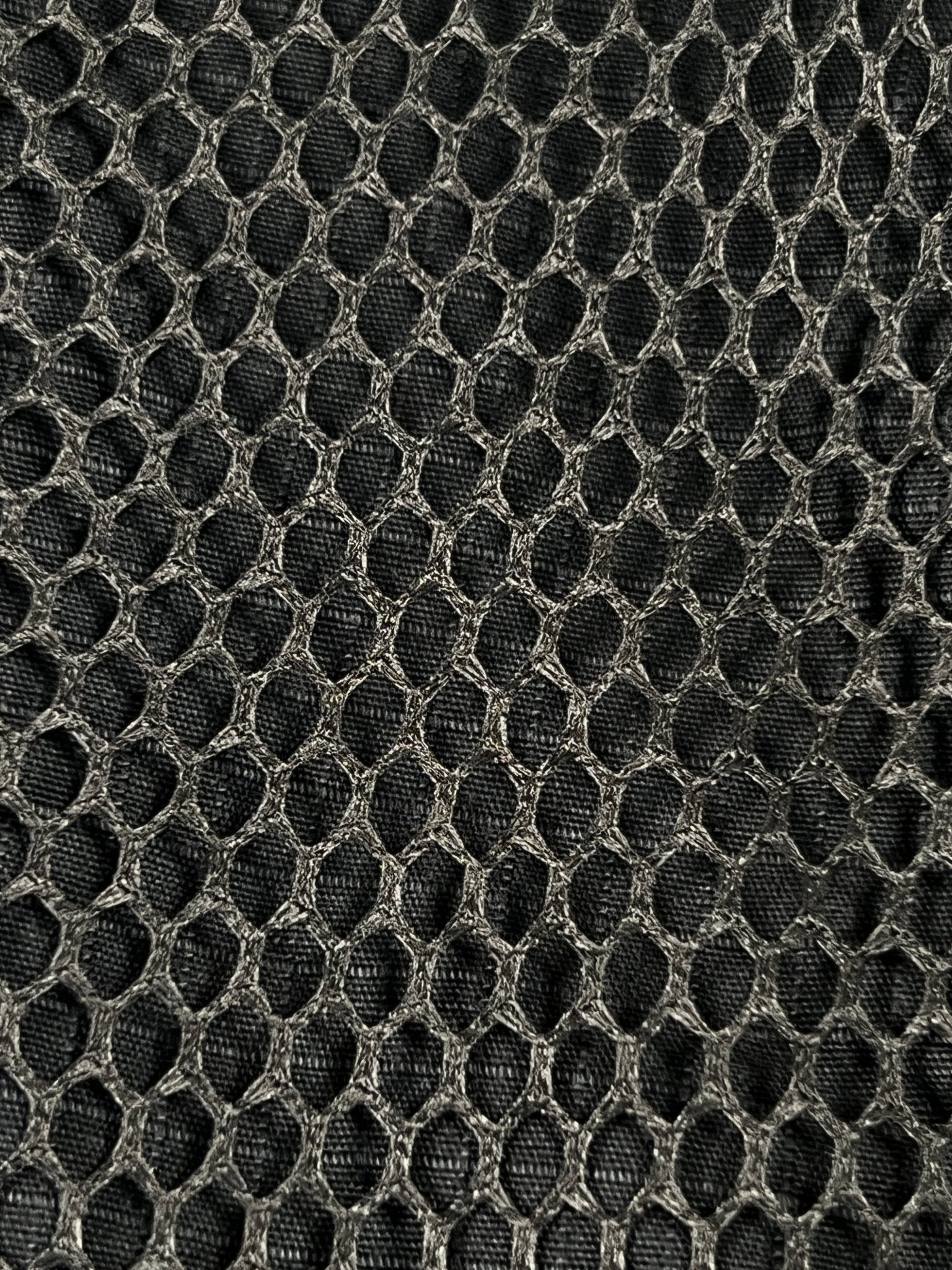 Close-up of black mesh fabric with a honeycomb pattern, featuring interlocking hexagons and textured detail—echoing the rugged style of DEVA'STATES Deva'States Hike Cargo Shorts Washed Black.