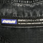 Close-up of a black fabric tag reading "GRAPHIC [グラフィック] GEAR" and "THIS GRAPHIC GARMENT MEETS/EXCEEDS TH," attached to DEVA'STATES Deva'States Hike Cargo Shorts in washed black cotton with a vintage washed finish.