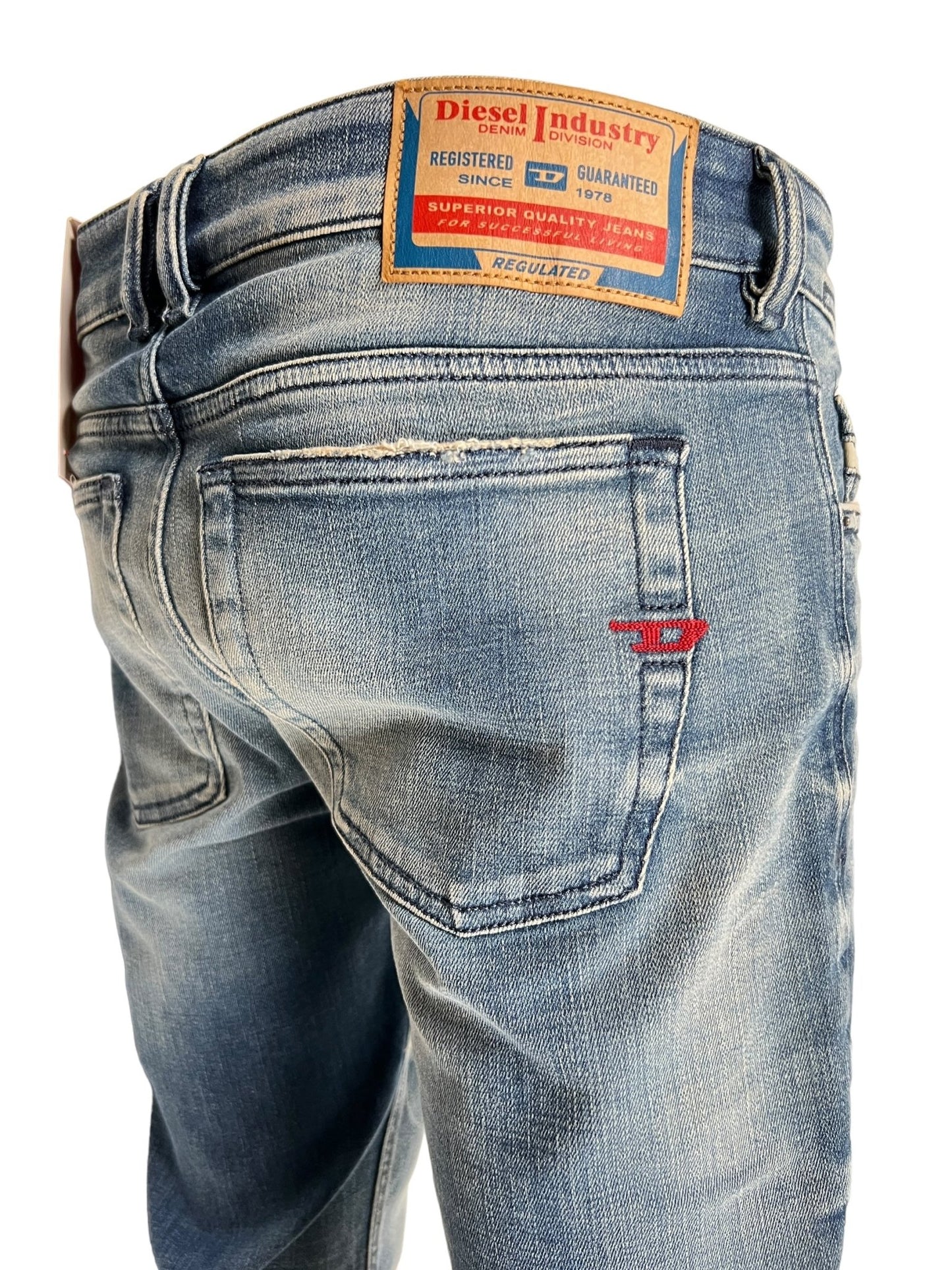 Rear view of a pair of DIESEL 1979 SLEENKER 9J24 medium blue stretch denim jeans with a punk-rock attitude, featuring a Diesel Industry brand label on the waistband and visible back pockets.