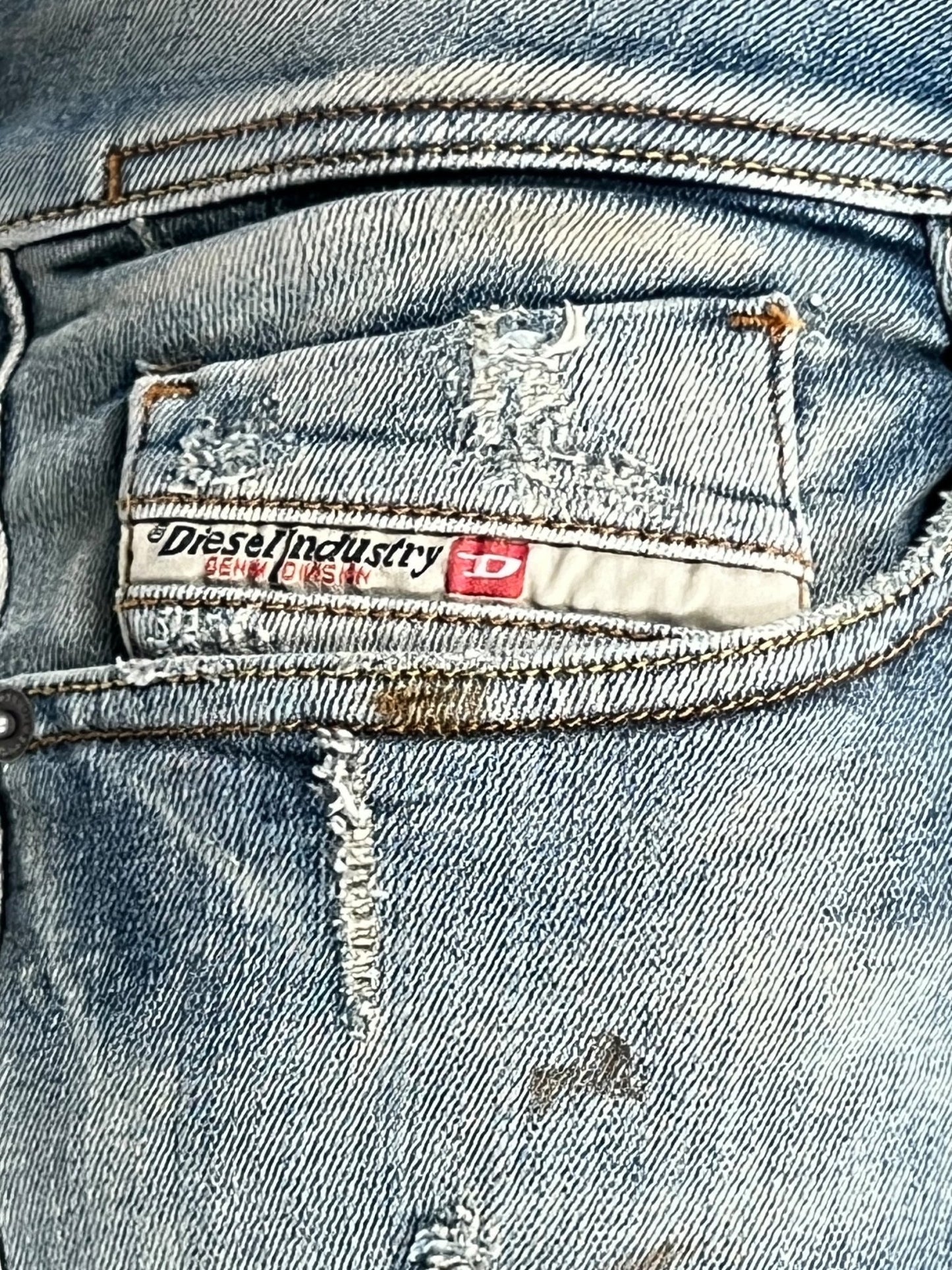 Close-up of a back pocket on the DIESEL 1979 SLEENKER 9J25 distressed blue skinny jeans, showcasing a Diesel Industry label with visible stitching and wear, emphasizing the punk-rock style.