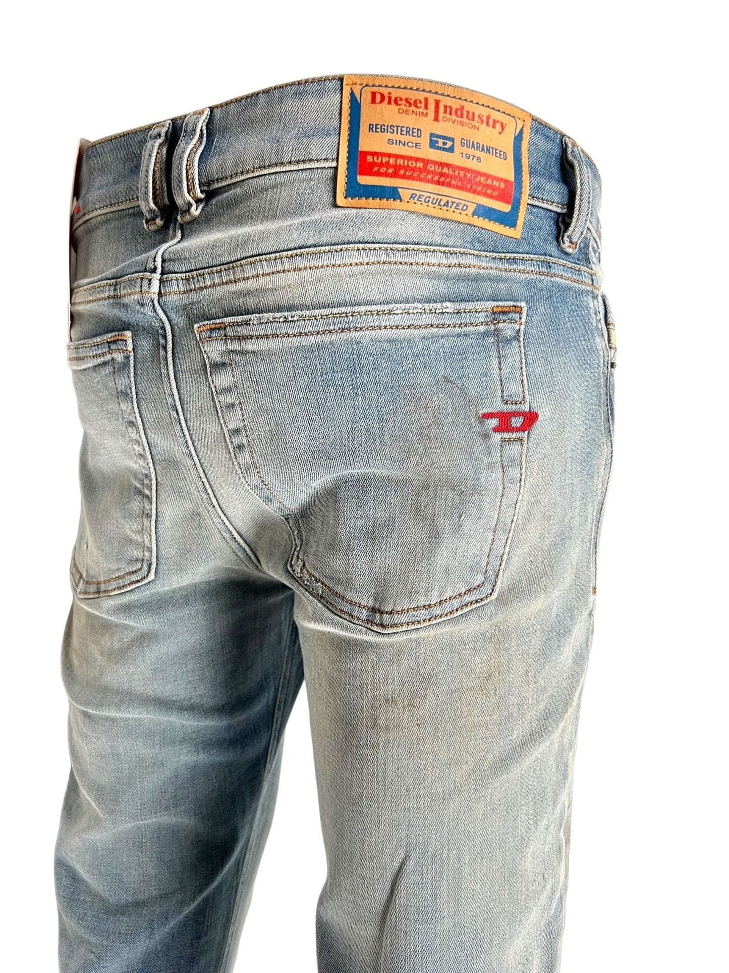 The DIESEL 1979 SLEENKER 9J25 denim skinny jeans feature a faded wash and a worn look with visible back pockets. Made from organic cotton denim, the back label reads "Diesel Industry." The jeans also include red stitching details on one pocket, adding a hint of punk-rock style.