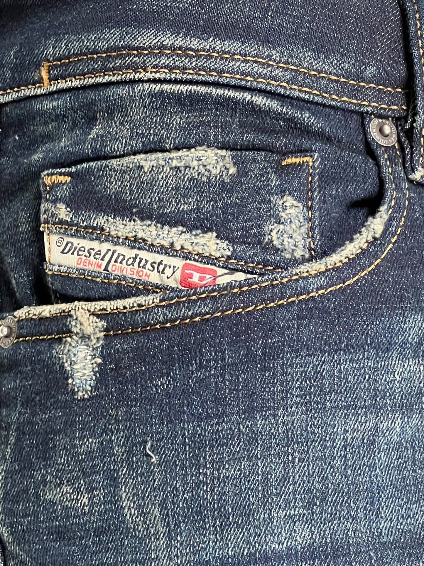 Close-up of the back pocket of a pair of distressed low waist blue DIESEL 1979 SLEENKER 9J26 jeans with the Diesel Industry label visible on the pocket.