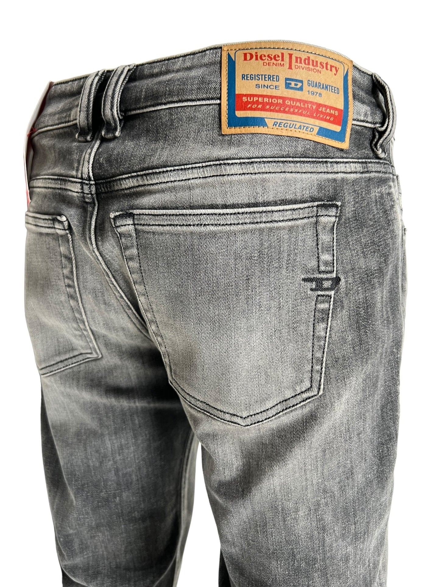 A close-up shot of the back of faded grey Diesel 1979 Sleenker 9J28 skinny fit jeans, featuring a tan leather patch on the waistband that reads "Diesel Industry 1979" along with additional brand information.