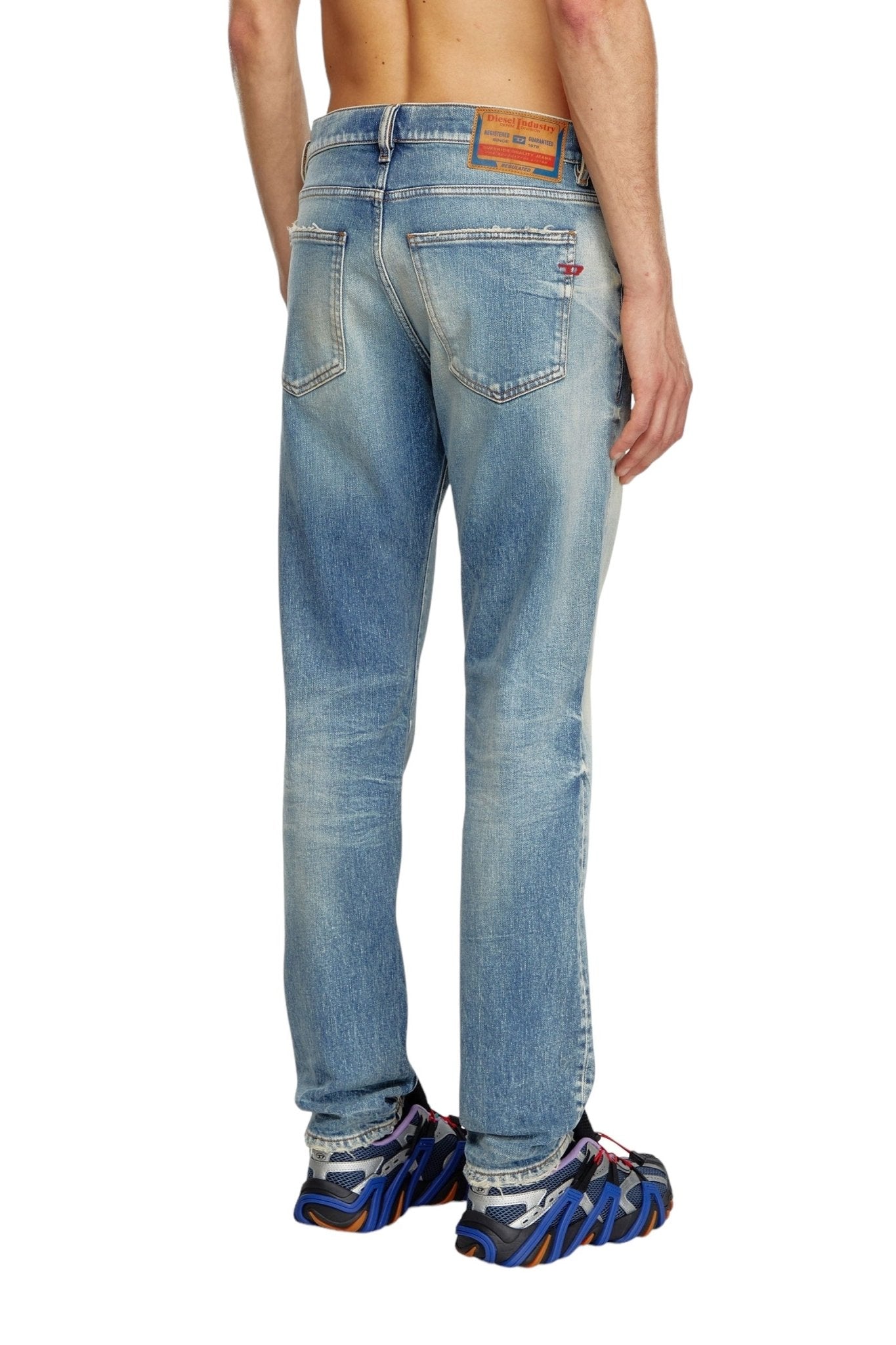 Back view of a person wearing the DIESEL 2019 D-STRUKT 07V8 slim jeans, made from organic cotton, featuring faded details and colorful sneakers. The jeans showcase visible stitching, back pockets, and a leather patch on the waistband.