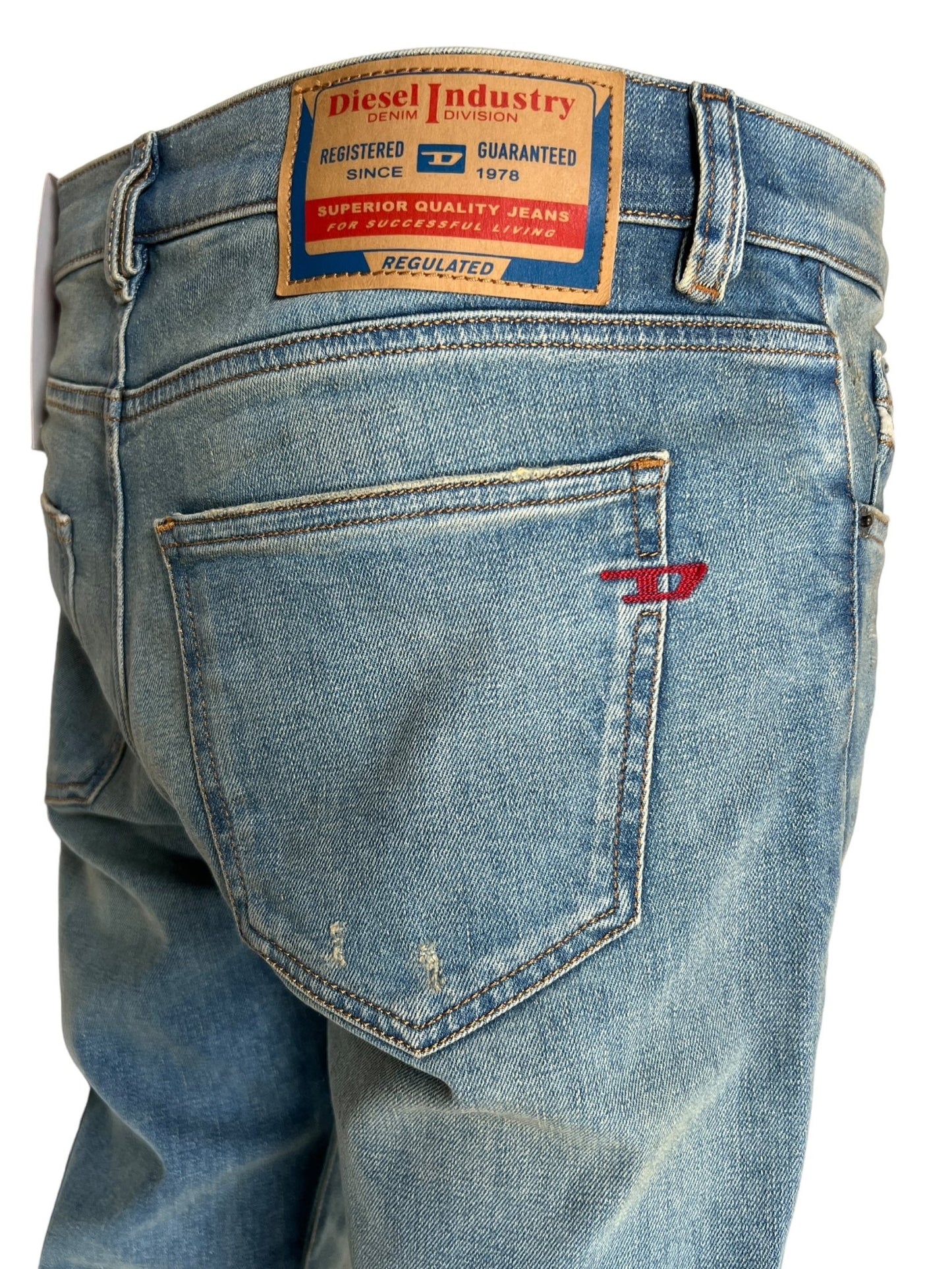 A close-up of the back of a pair of DIESEL 2019 D-STRUKT 9H50 DENIM with a tan DIESEL Industry brand label above the right pocket and a small red "D" logo embroidered on the pocket, crafted using recycled cotton.