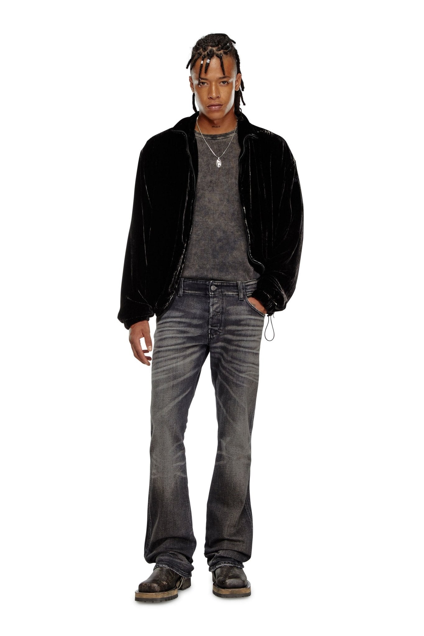 A person with braided hair stands wearing a black jacket, dark shirt, DIESEL comfort denim bootcut jeans (D-BACKLER-RR 9J65), and black shoes, against a white background.