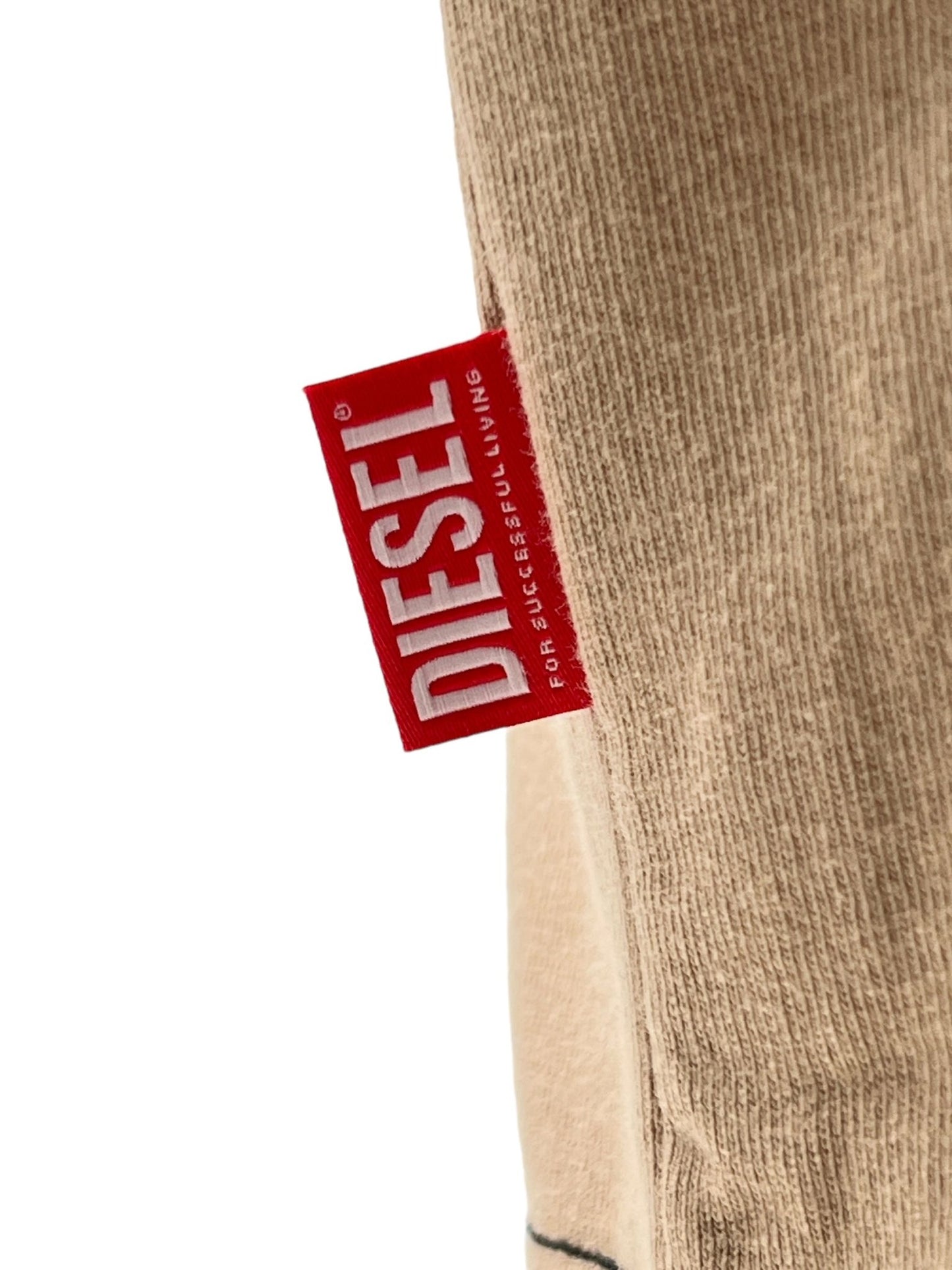 A close-up of a red Diesel brand tag attached to a beige fabric. Text on the tag reads "DIESEL For Successful Living." The tag adorns one of the stylish DIESEL T-ADJUST-Q1 T-SHIRT 72S, known for its regular fit and quality craftsmanship.