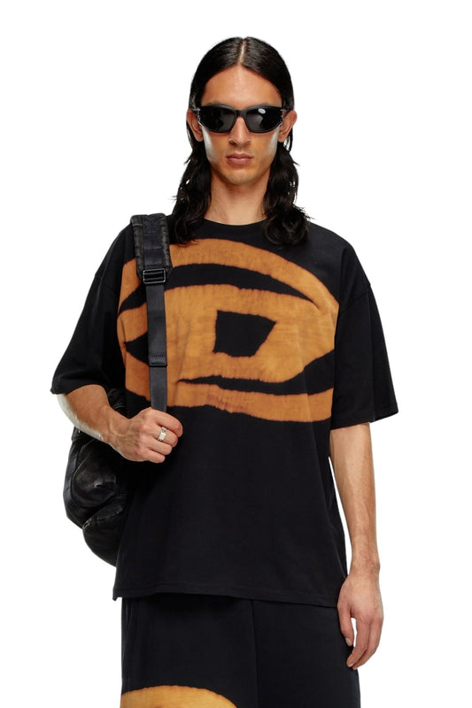 A person with long hair, wearing sunglasses, a DIESEL T-BOXT-BLEACH T-SHIRT BLACK with an Oval D logo, and carrying a black backpack.