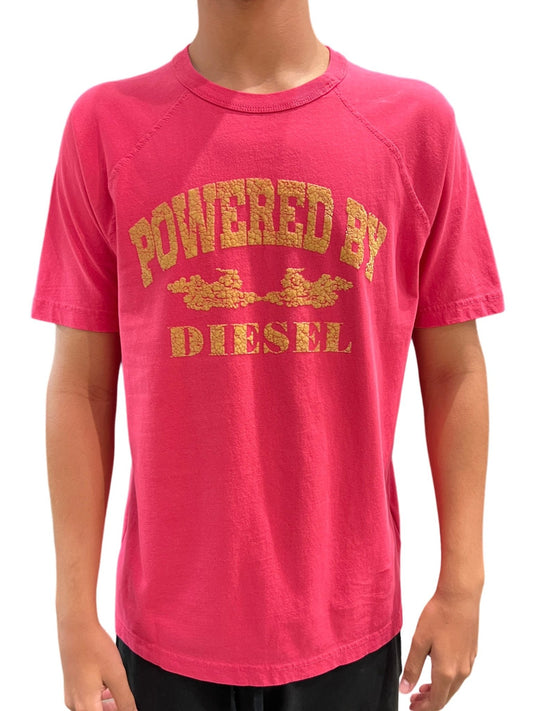 Person wearing a pink DIESEL T-RUST t-shirt with the phrase "powered by diesel" printed in gold lettering.