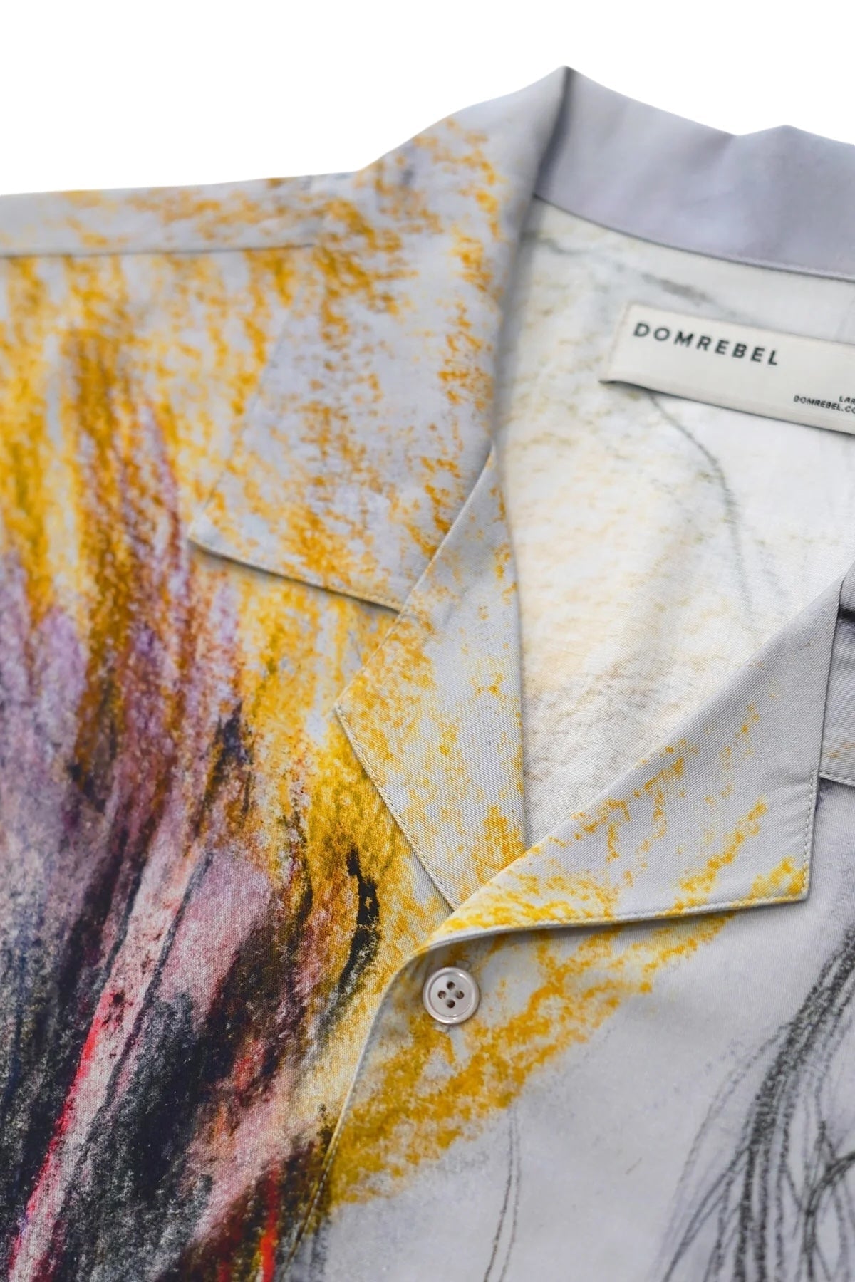 Close-up of a Domrebel Ascend Camp Collar Shirt Beige with an abstract design featuring yellow, red, and gray tones crafted from twill fabric. The label reads "DOM REBEL," showcasing original studio artworks.