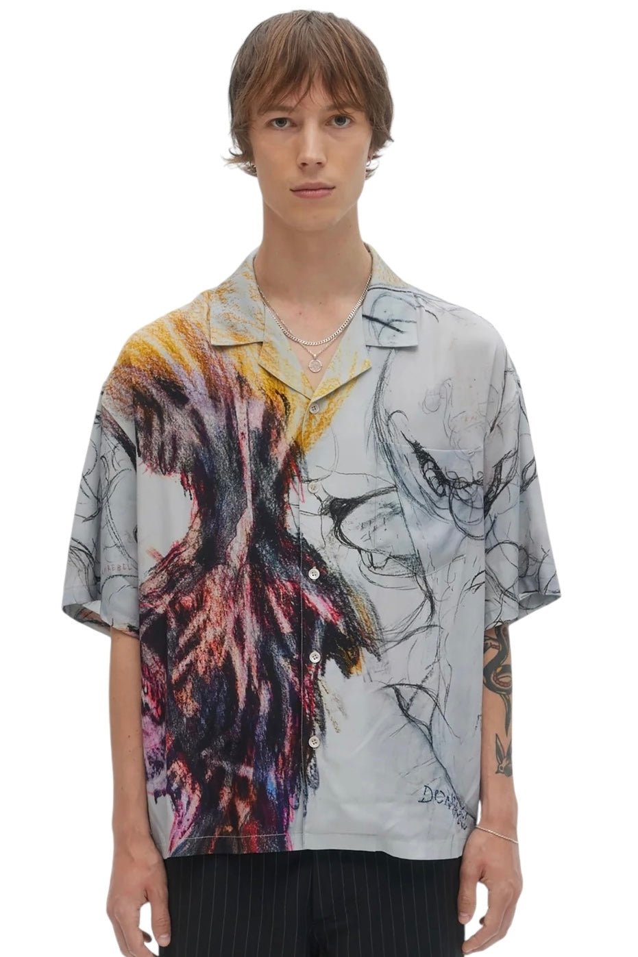 A person wearing the Domrebel Ascend Camp Collar Shirt in beige from DOM REBEL, featuring a colorful abstract pattern, and dark pants stands facing forward.