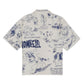 The Domrebel Bearing Camp Collar Shirt Beige by DOM REBEL showcases an all-over print with blue graphic designs and text set against a crisp white backdrop, crafted from a soft Rayon Tencel blend. This short-sleeve shirt combines style and comfort, making it perfect for any casual outing.