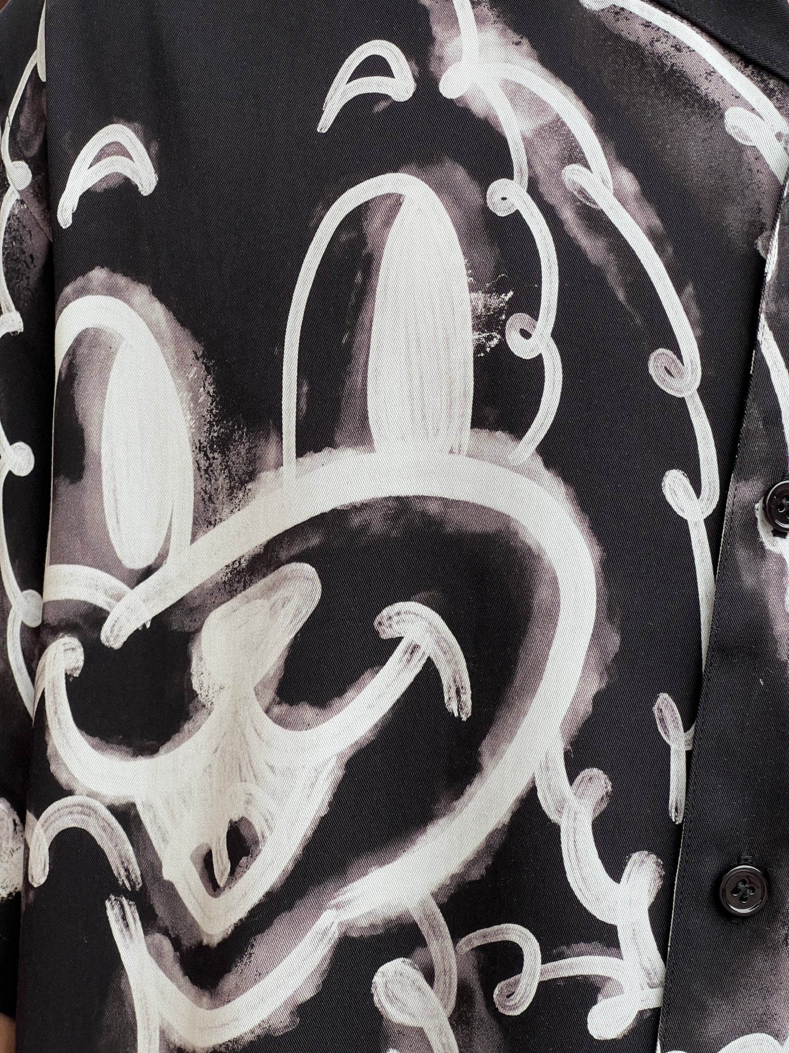 Close-up of a DOM REBEL DOMREBEL CHAINED SHIRT BLACK with a black all-over print featuring a white graffiti-style drawing of a cartoon face. The design showcases large eyes and a wide smile, bringing playful charm to the rayon Tencel blend fabric.