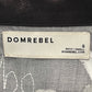 Label of a DOM REBEL DOMREBEL CHAINED SHIRT BLACK, highlighting the brand name, the size "S", and the website "DOMREBEL.COM". The tag also features the word "PETIT/SMALL" to denote its small size.