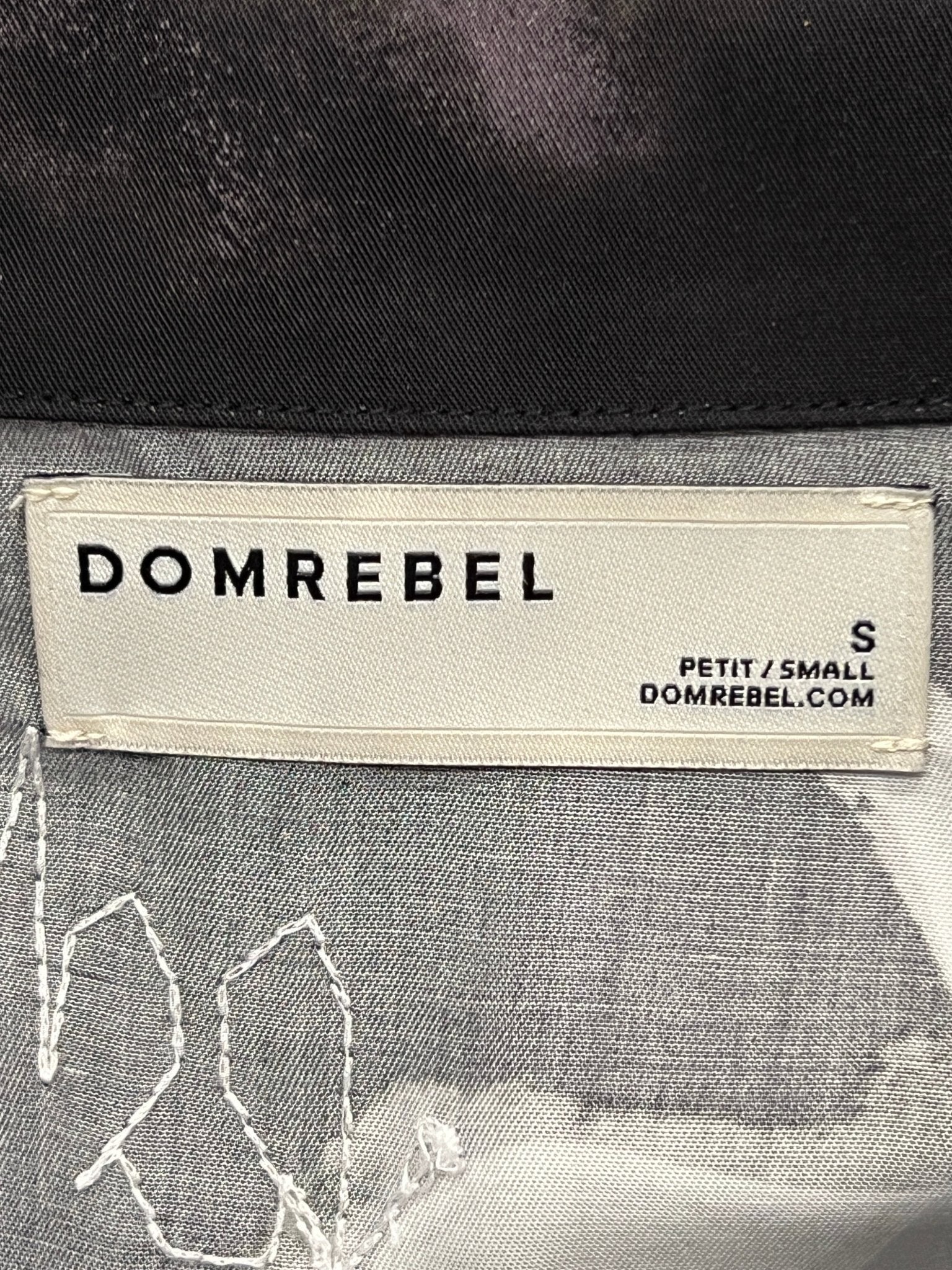 Label of a DOM REBEL DOMREBEL CHAINED SHIRT BLACK, highlighting the brand name, the size "S", and the website "DOMREBEL.COM". The tag also features the word "PETIT/SMALL" to denote its small size.