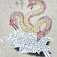 The Domrebel Conflict T-shirt Greige by DOM REBEL showcases an original doodle of a three-headed dragon in red accents with "CONCRETE" text and sparkles, creating a standout piece for any collection.