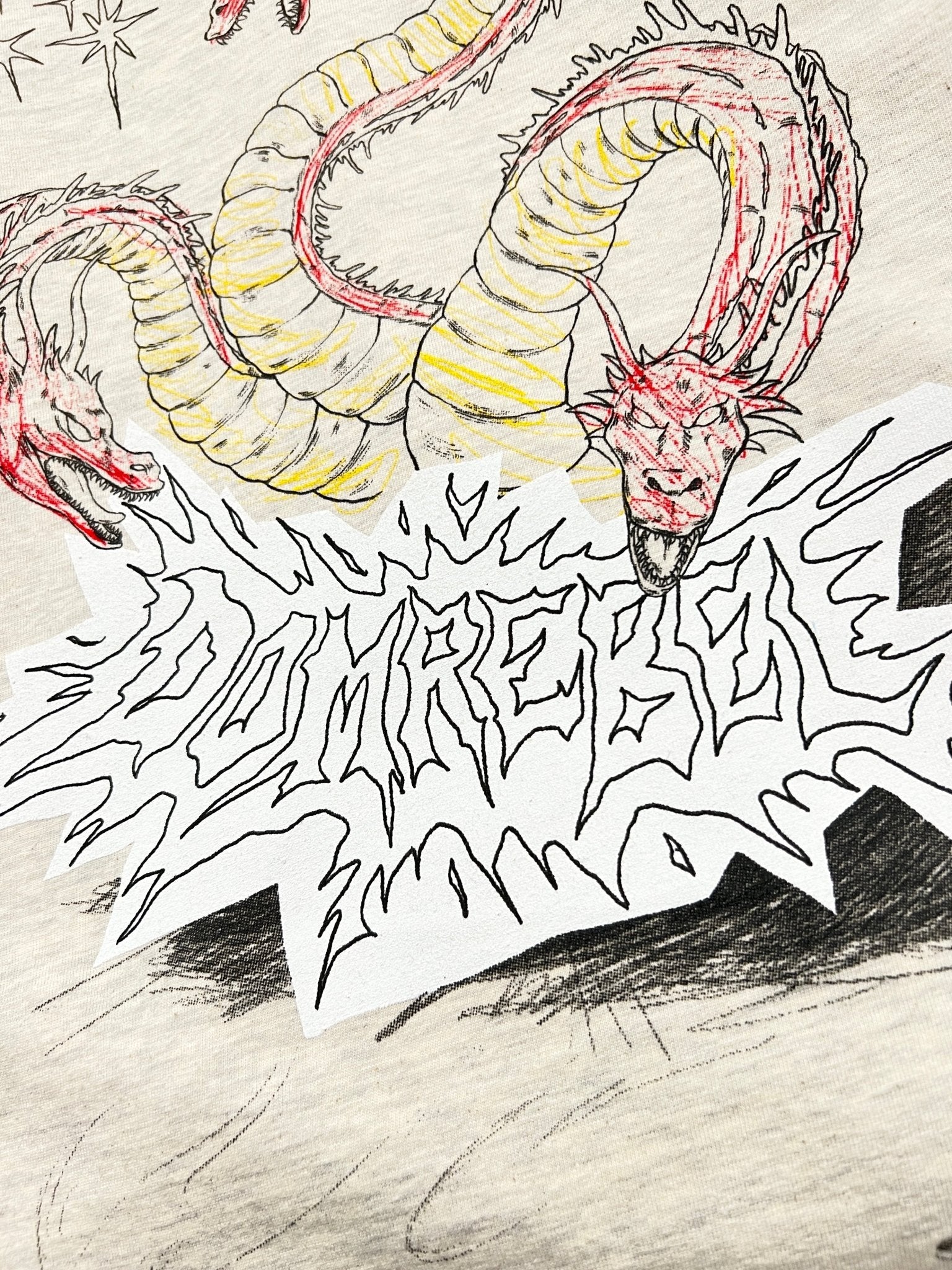 A two-headed dragon illustration above the stylized "DOMREBEL" text features an original doodle graphic on a greige background. This design adorns the premium Domrebel Conflict T-shirt Greige by DOM REBEL, blending fantasy and fashion.