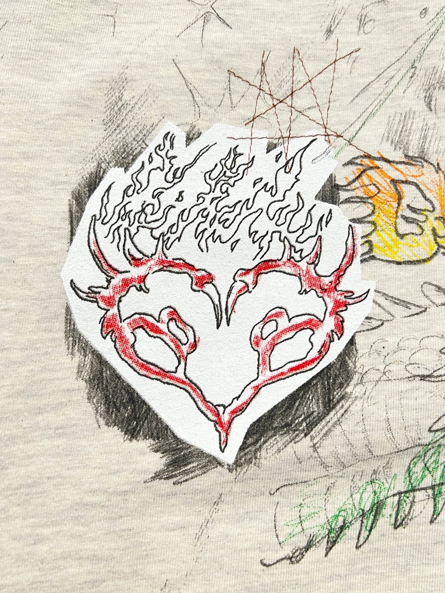 The Domrebel Conflict T-shirt Greige from Dom Rebel features the iconic doodle graphic, displaying a sketched red heart with flame-like edges and horns amidst abstract scribbles and shapes.