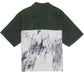 The Domrebel Demi Camp Collar Shirt by DOM REBEL blends style and comfort with its split design: solid dark green on the top, abstract black and gray scribbles on white below. Made from twill fabric, it reflects classic DOMREBEL sketches.