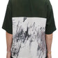 A person wearing the Domrebel Demi Camp Collar Shirt Green by DOM REBEL, featuring a twill fabric with a dark green top and an abstract black-and-white lower design, seen from the back.