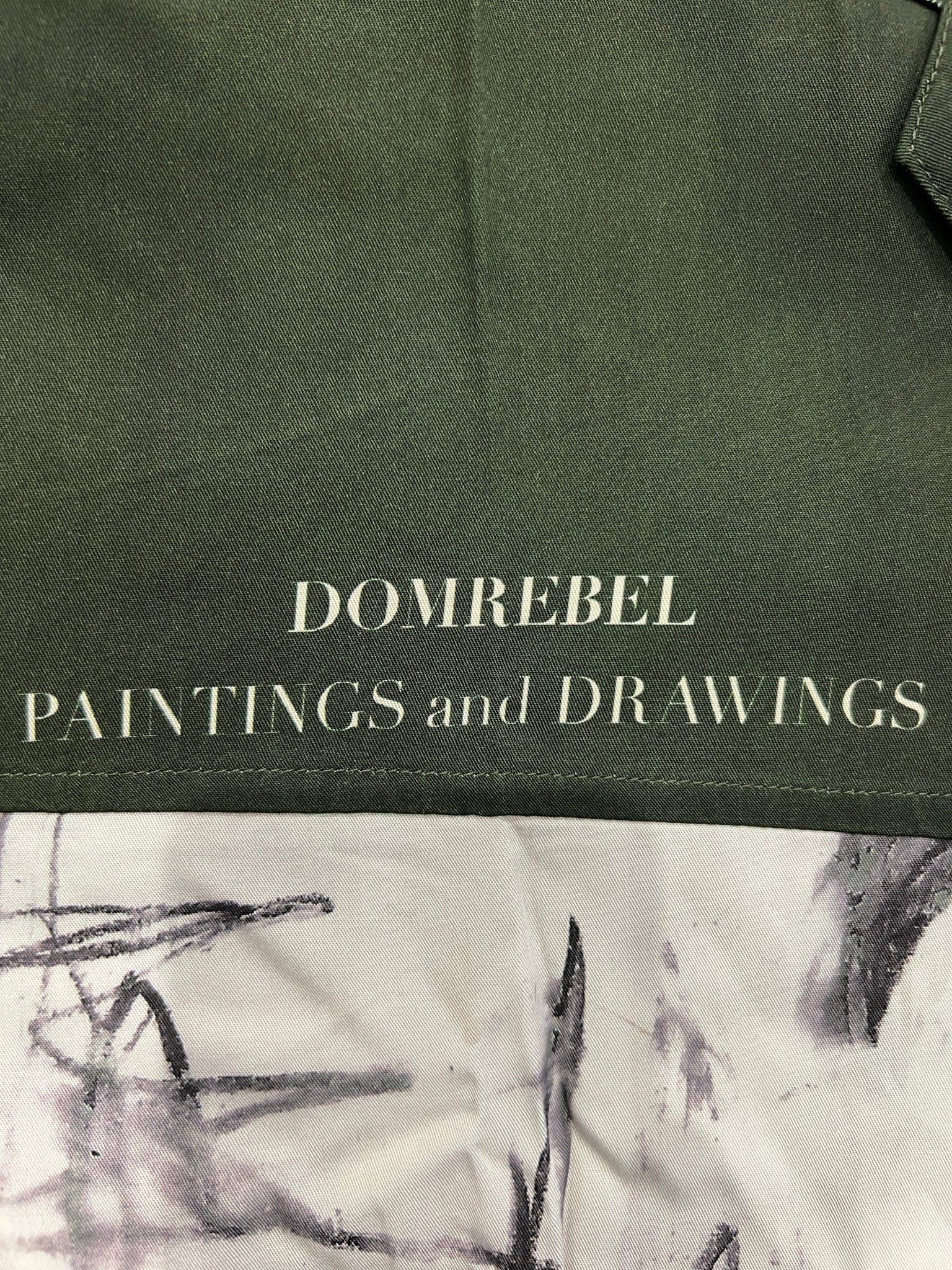 Close-up of a twill fabric with "DOMREBEL PAINTINGS and DRAWINGS" printed on it, featuring abstract brush strokes. This eye-catching design could turn the Domrebel Demi Camp Collar Shirt Green by DOM REBEL into a vibrant canvas of artistic sketches.