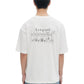 A person wearing a Domrebel Friendly T-Shirt Ivory with a comic-style teddy bear pairs it with blue splattered jeans, viewed from the back—perfect for those who love the eclectic style of the DOM REBEL bon vivant collection.