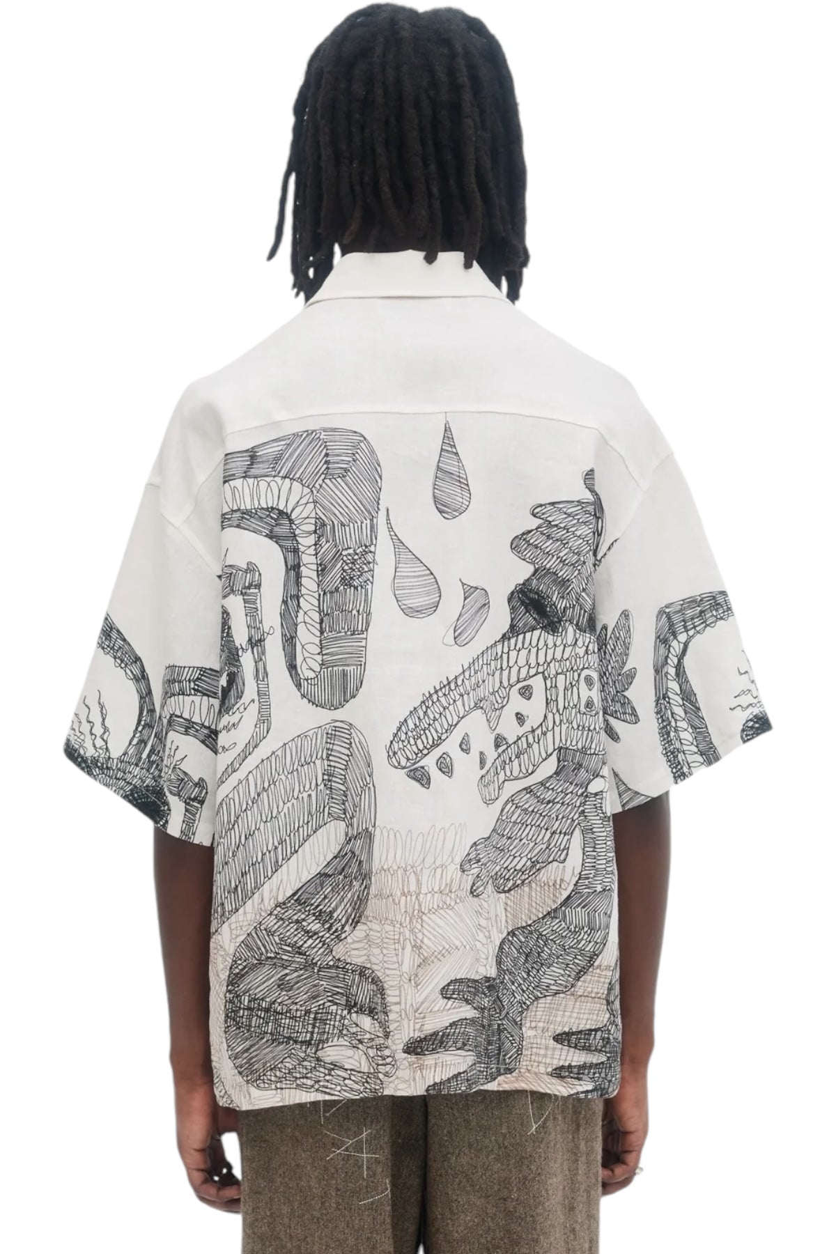 A person wearing the Domrebel Hao Shirt in beige by DOM REBEL, featuring a black abstract pattern on the back that resembles graphite character drawings, stands against a white background.